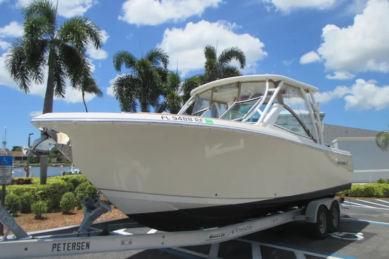 The Image of 2017 Sailfish 275 DC boat on trailer, parked under palm trees, clear blue sky. - 0
