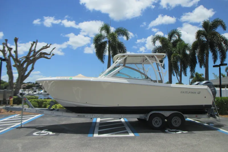 Slide: The Image of 2017 Sailfish 275 DC boat on trailer, parked under clear blue sky with palm trees. - 1