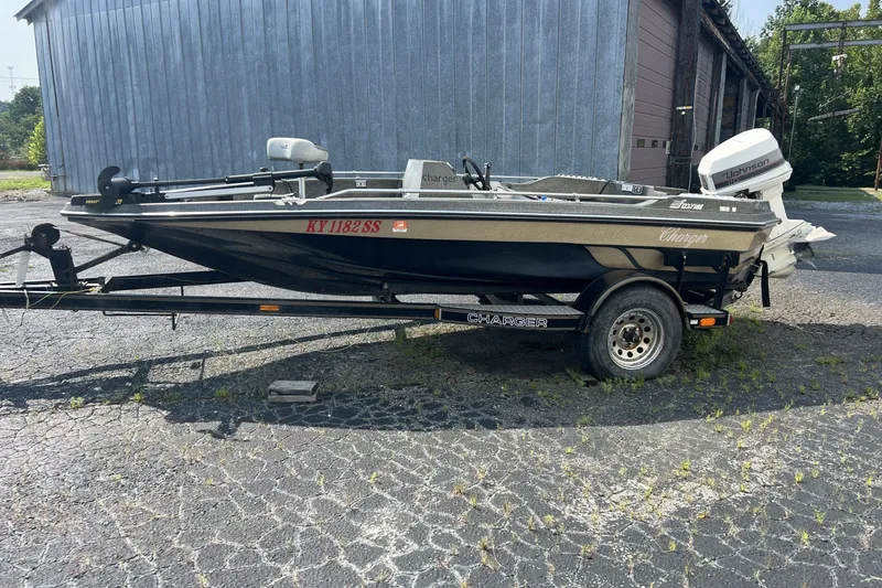 Slide: The Image of 1988 Charger 162V boat on trailer, parked outdoors near a metal building. - 2