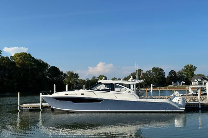 The Image of 2024 Pursuit OS 445 Offshore yacht docked on a serene lake under a clear blue sky. - 0