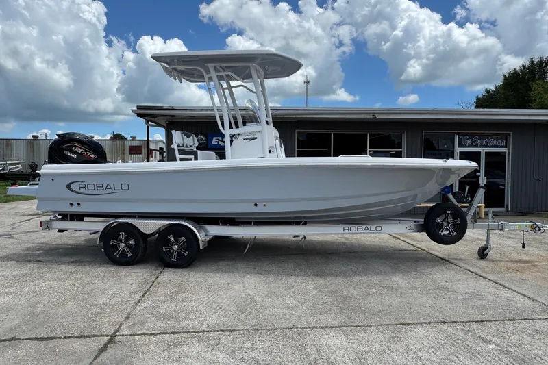 The Image of 2026 Robalo 226 Cayman boat on trailer, parked outdoors under cloudy sky. - 1