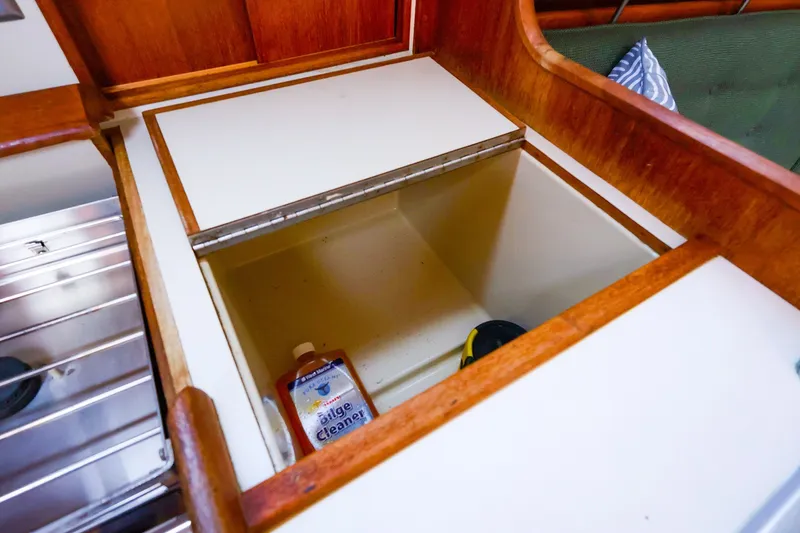 Slide: The Image of Interior storage compartment on a 1990 Ericson 32.5 sailboat, featuring wooden trim and cleaning supplies. - 29
