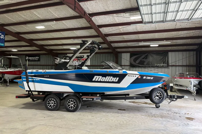 The Image of 2023 Malibu Wakesetter 21 LX boat in a showroom, featuring a sleek blue and white design. - 0
