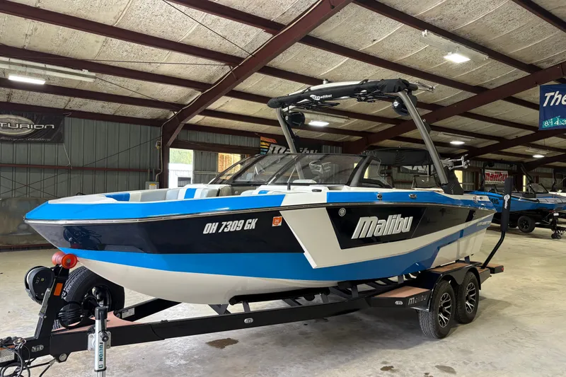 Slide: The Image of 2023 Malibu Wakesetter 21 LX boat in a showroom, featuring a sleek blue and white design. - 6