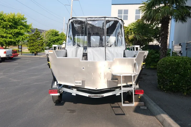 Slide: The Image of 2026 Hewescraft 180 Sportsman boat, rear view, parked outdoors near greenery. - 6