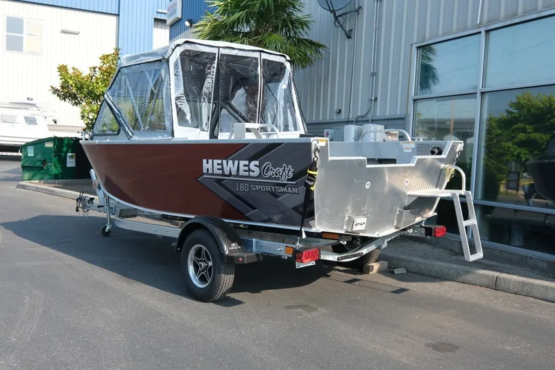 Slide: The Image of 2026 Hewescraft 180 Sportsman boat on trailer, parked outdoors near industrial building. - 5