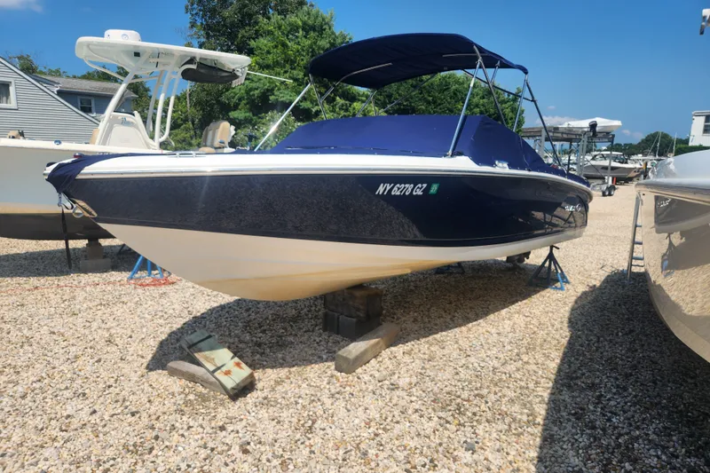 Slide: The Image of 2012 Cobalt 220 boat on gravel, covered and elevated, with nearby trees and buildings. - 1