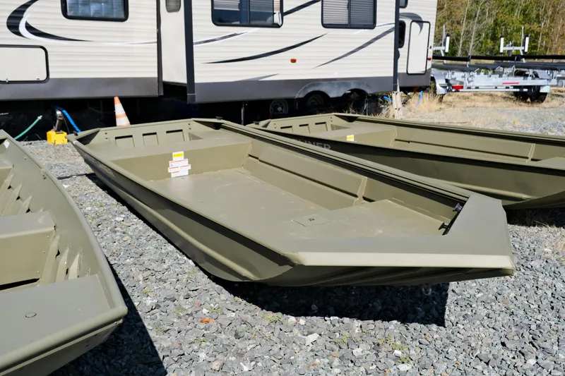 The Image of A 2024 Crestliner 1546 Retriever, a sturdy aluminum boat, sits on gravel next to a trailer. - 1