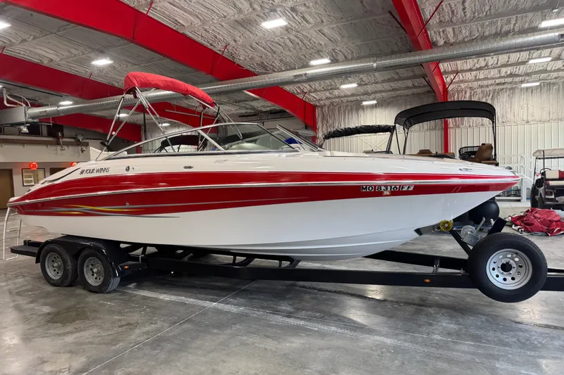 The Image of 2005 Four Winns 250 Horizon boat with red accents on a trailer in a warehouse. - 1