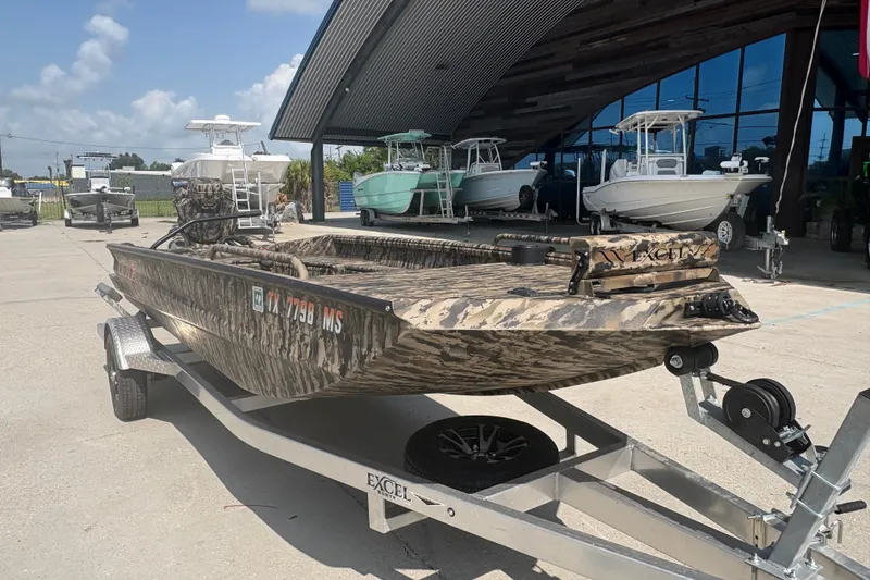 Slide: The Image of 2026 Excel 1751 Shallow Water F4 boat on trailer, camo design, outdoor showroom. - 11