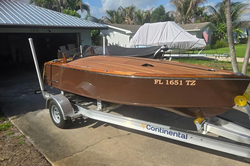 The Image of 2025 Florida Custom Boats 17 on trailer, parked in driveway, with wooden deck and brown hull. - 0