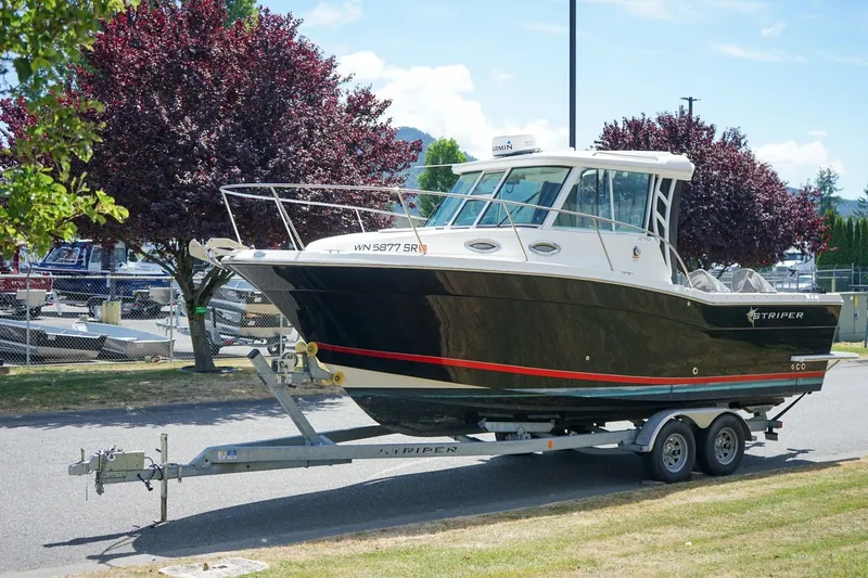 Slide: The Image of 2019 Striper 270 Walkaround boat on trailer, parked outdoors near trees. - 19
