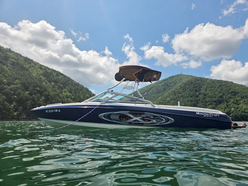 The Image of A 2003 MasterCraft X-30 boat floats on a calm lake, surrounded by green hills. - 1