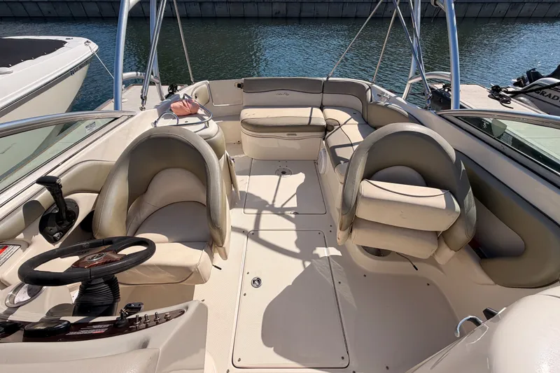 Slide: The Image of 2005 Sea Ray 240 Sundeck boat interior with seating and steering wheel, docked by the water. - 23
