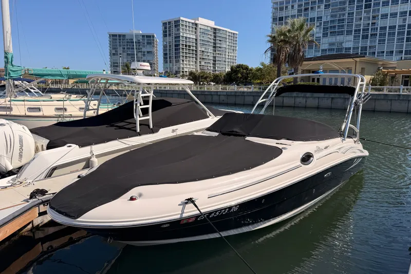 Slide: The Image of 2005 Sea Ray 240 Sundeck boat docked in a marina with modern buildings in the background. - 1