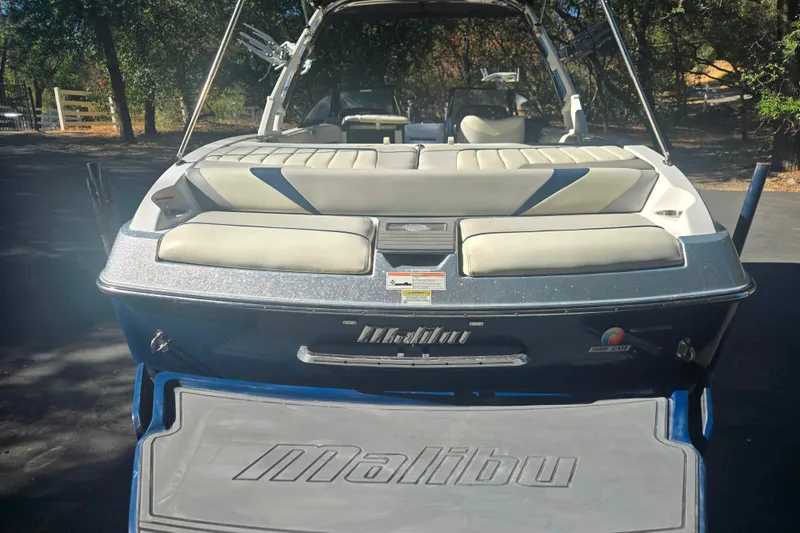 Slide: The Image of 2013 Malibu Wakesetter 24 MXZ boat with cushioned seating, parked outdoors. - 18