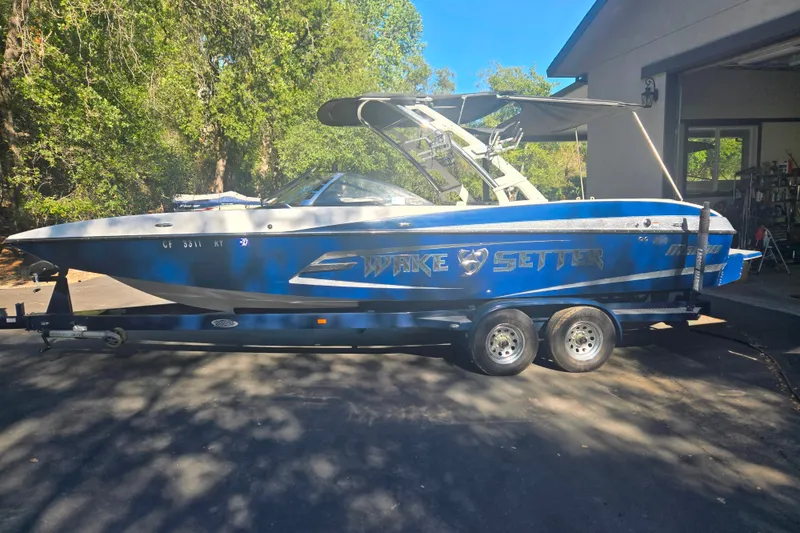 Slide: The Image of 2013 Malibu Wakesetter 24 MXZ boat on trailer, parked outdoors near trees. - 17