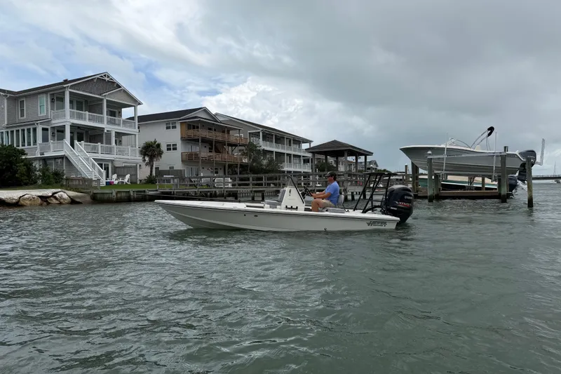 Slide: The Image of 2020 Hewes Redfisher 18 boat cruising near waterfront homes under cloudy skies. - 11