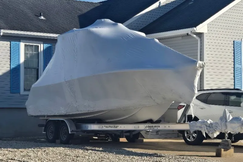 Slide: The Image of 2023 Sailfish 245 DC boat covered on trailer beside house. - 2