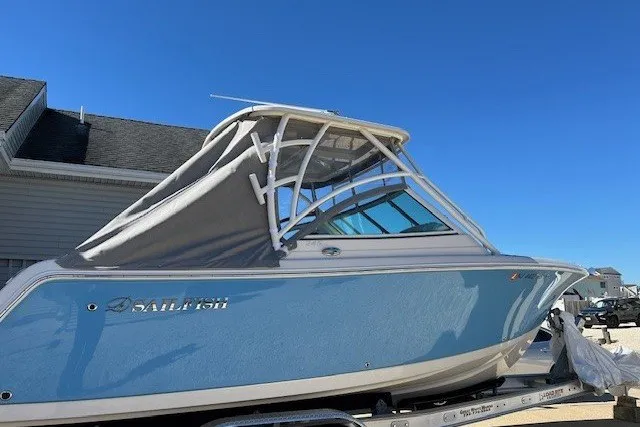 Slide: The Image of 2023 Sailfish 245 DC boat with blue hull and canopy, parked on a trailer. - 1