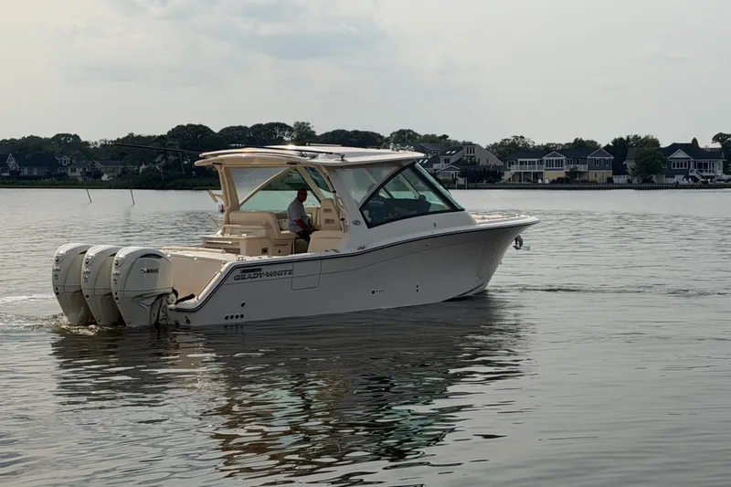 Slide: The Image of 2027 Grady-White Freedom 345 boat cruising on calm waters near residential shoreline. - 7