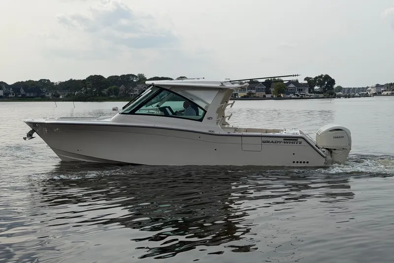 Slide: The Image of 2027 Grady-White Freedom 345 boat cruising on calm waters near shoreline homes. - 2