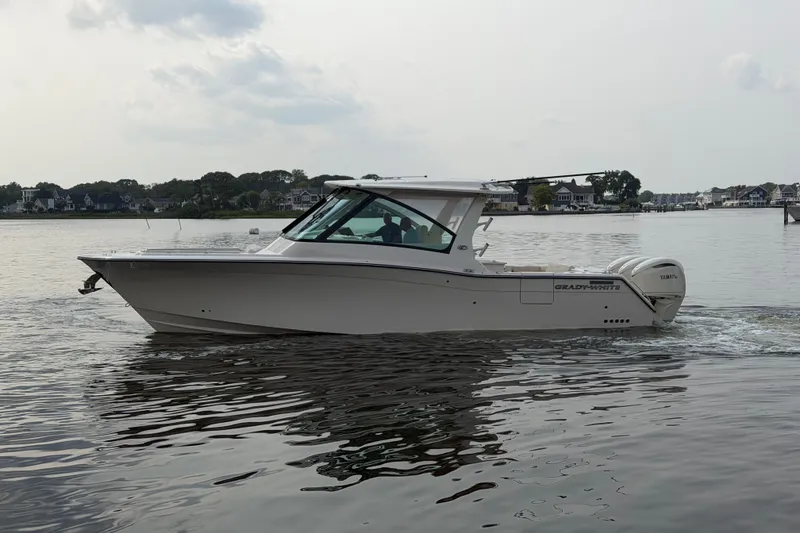 Slide: The Image of 2027 Grady-White Freedom 345 boat cruising on calm waters near a residential shoreline. - 1