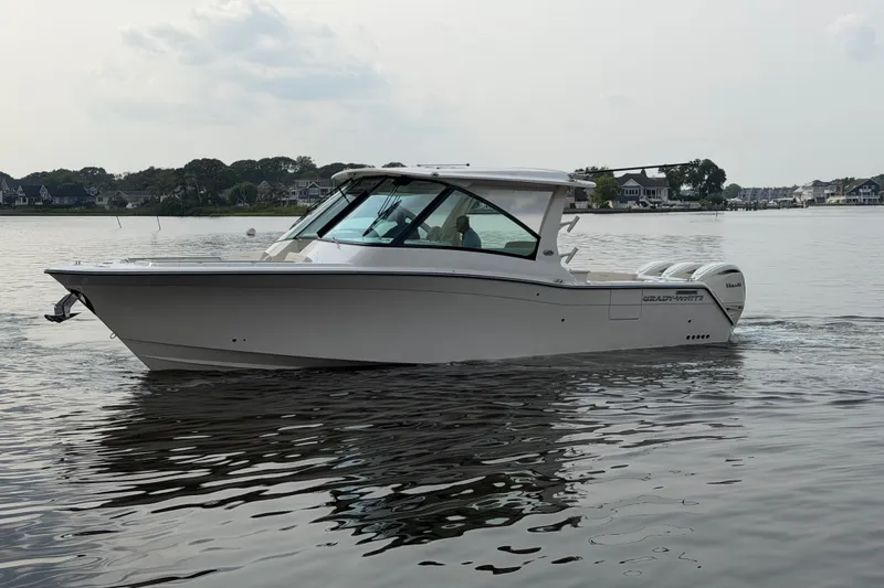 The Image of 2027 Grady-White Freedom 345 boat cruising on calm waters near a residential shoreline. - 0