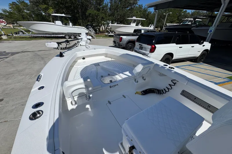 Slide: The Image of 2025 BlackJack 256 Coastal boat interior with seating and fishing equipment, parked near vehicles. - 17