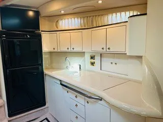 Slide: The Image of The 1999 Sea Ray 410 Express Cruiser's kitchen features white cabinets and a black fridge-freezer. - 18