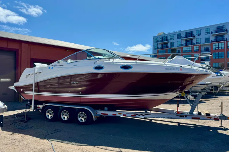 Slide: The Image of 2006 Searay 260 boat on trailer, parked outdoors near a building under a clear blue sky. - 0