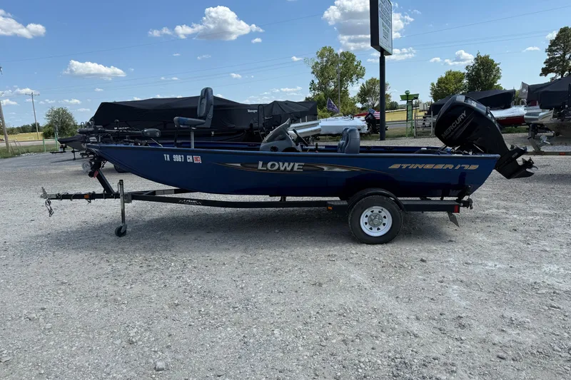 Slide: The Image of 2014 Lowe Stinger 175 boat on trailer, parked outdoors under a blue sky. - 1