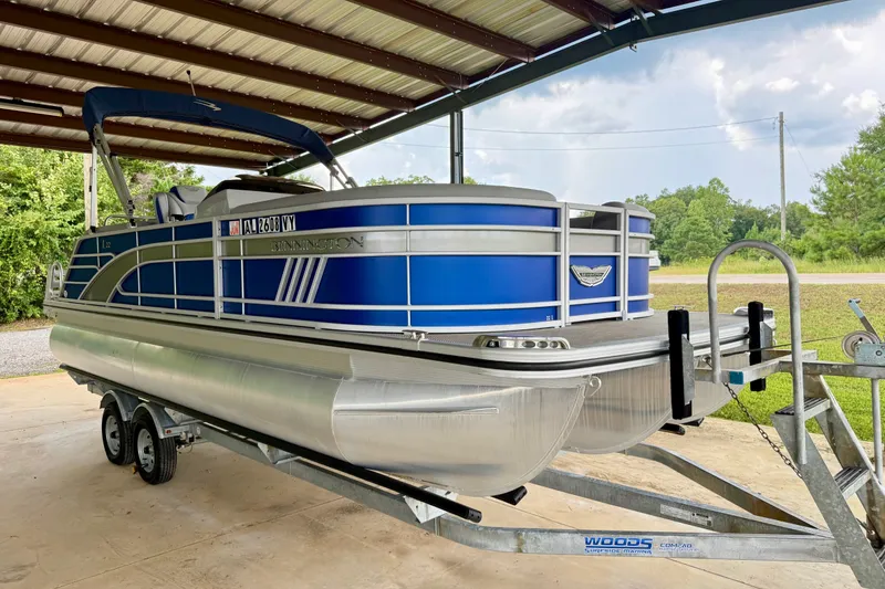 Slide: The Image of 2024 Bennington L22 pontoon boat on trailer under metal canopy. - 6