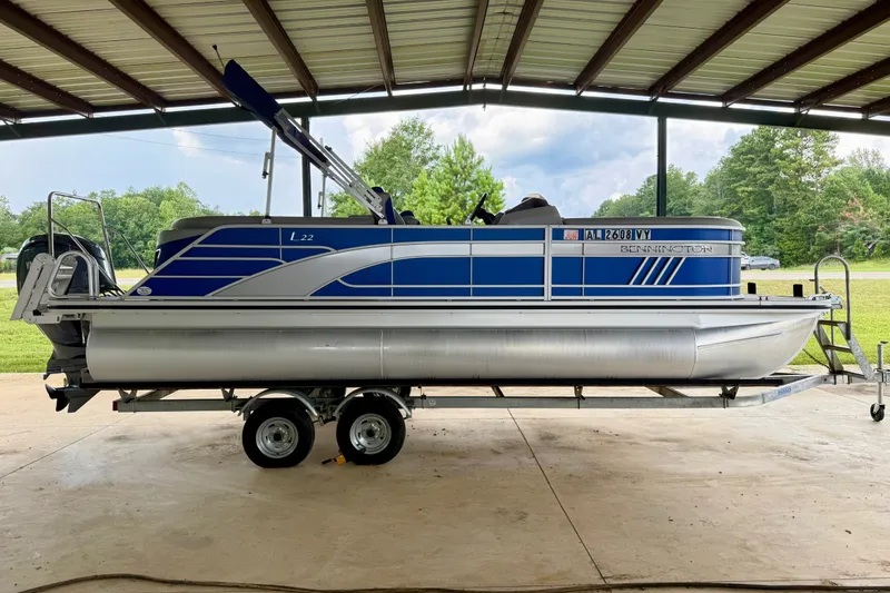 Slide: The Image of 2024 Bennington L22 pontoon boat on trailer under a metal roof, side view. - 5