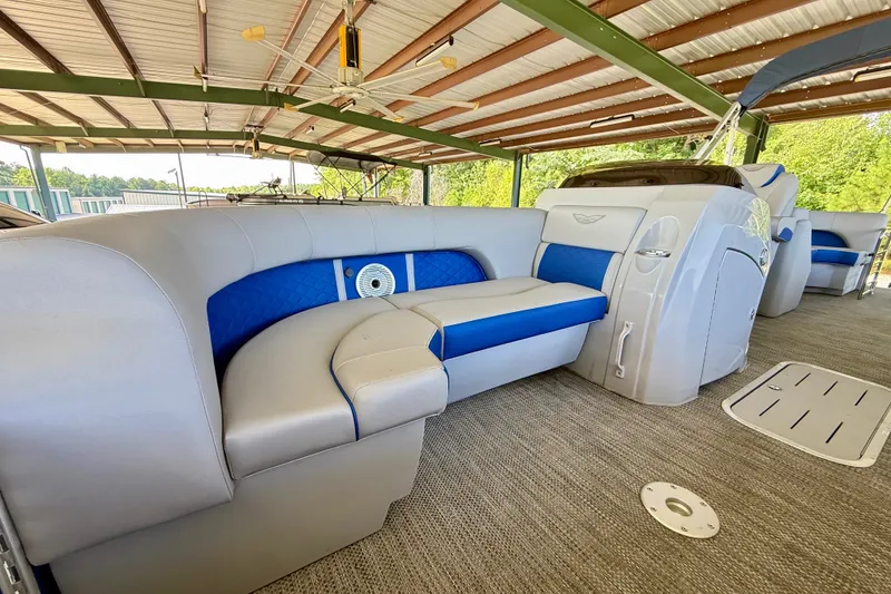 Slide: The Image of 2024 Bennington L22 pontoon boat interior with blue and gray seating under a covered dock. - 22