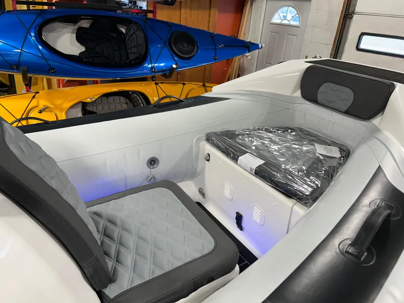 Slide: The Image of 2025 Highfield Sport 420 boat interior with cushioned seating and storage, kayaks in background. - 11