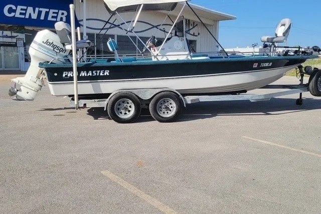 The Image of 1999 ProMaster 220 Bay boat on trailer, parked outdoors, featuring Johnson outboard motor. - 0