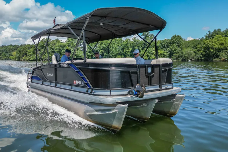 Slide: The Image of 2021 Godfrey Monaco 235 pontoon boat cruising on a scenic lake under a clear blue sky. - 0