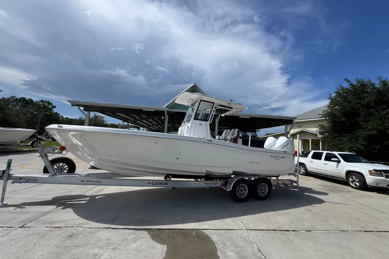 Slide: The Image of 2027 Caymas 291 boat on trailer under cloudy sky, parked near vehicles. - 2