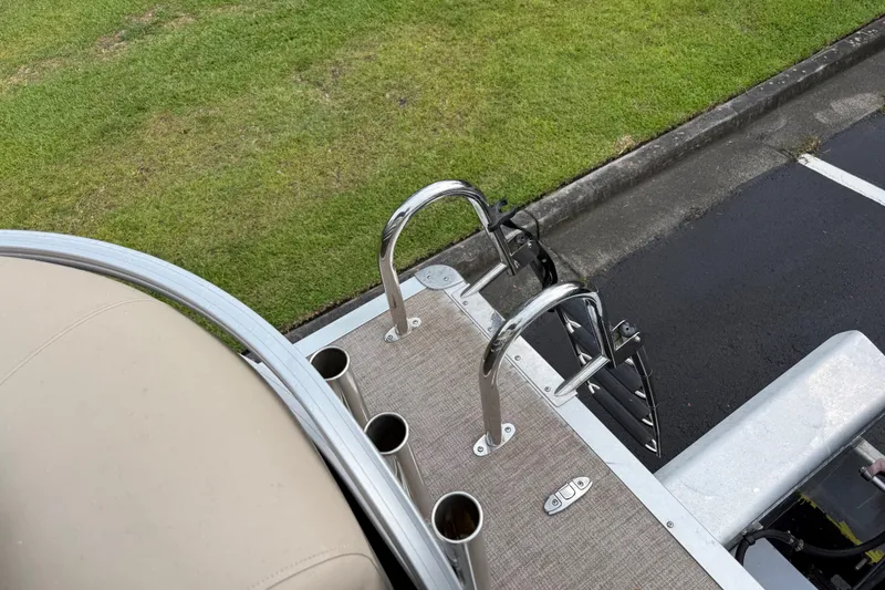 Slide: The Image of 2023 Sun Tracker Party Barge 22 XP3 boat ladder and deck, parked on grass. - 22