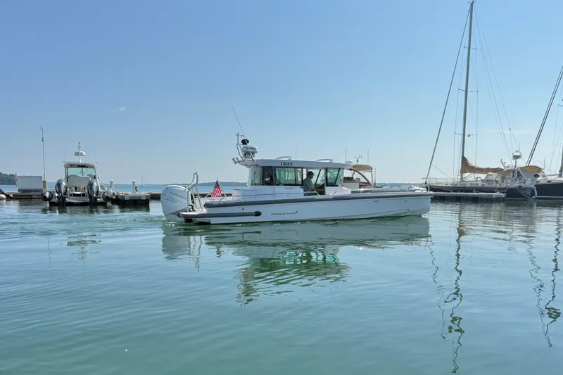 Slide: The Image of 2022 Axopar 28 Cabin boat cruising near marina with sailboats in background. - 41