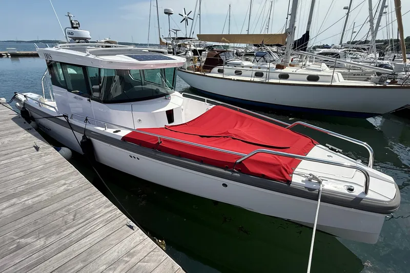 Slide: The Image of 2022 Axopar 28 Cabin boat docked with red cover, surrounded by sailboats. - 2