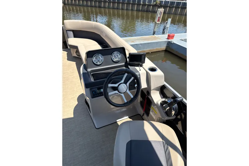 Slide: The Image of 2024 Harris Cruiser 230 boat interior with steering wheel and dashboard, docked by the water. - 5