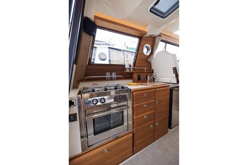 Slide: The Image of 2026 Ranger Tugs R-27 interior kitchen with stove, wooden cabinetry, and modern design. - 19