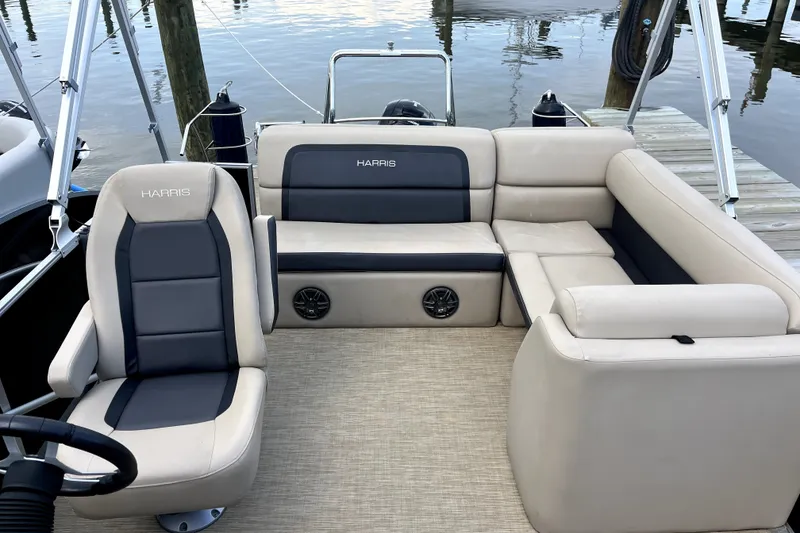 Slide: The Image of 2024 Harris Cruiser 230 boat interior with beige and black seating, docked by the water. - 4
