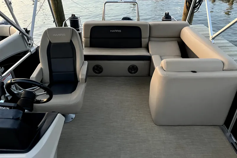 Slide: The Image of 2024 Harris Cruiser 230 boat interior with beige seating and steering wheel, dockside view. - 8
