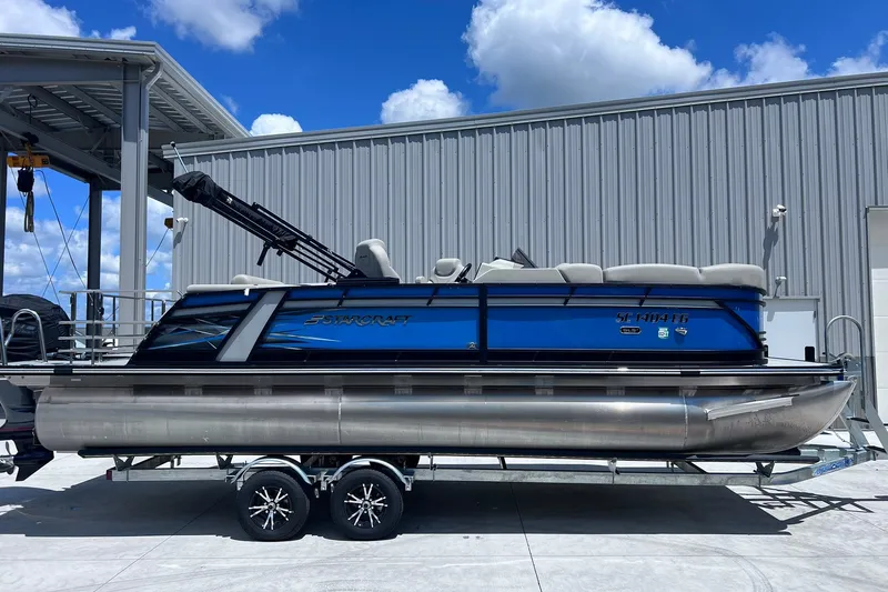 The Image of 2024 Starcraft SLS 3 pontoon boat on trailer, parked outdoors under blue sky. - 1