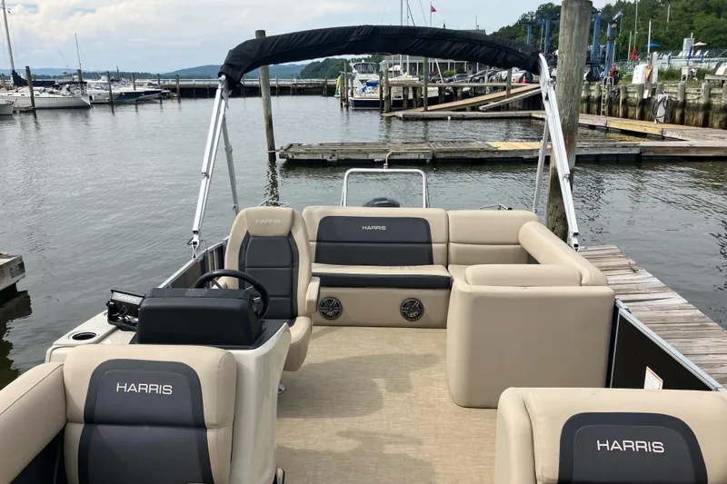 Slide: The Image of 2024 Harris Cruiser 230 pontoon boat docked at a marina, featuring spacious seating. - 5