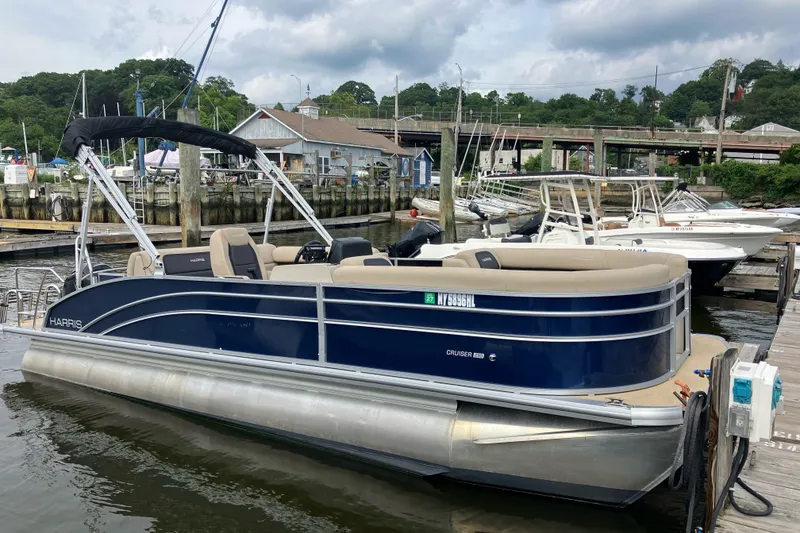 The Image of 2024 Harris Cruiser 230 pontoon boat docked at a marina, featuring sleek design and comfortable seating. - 1