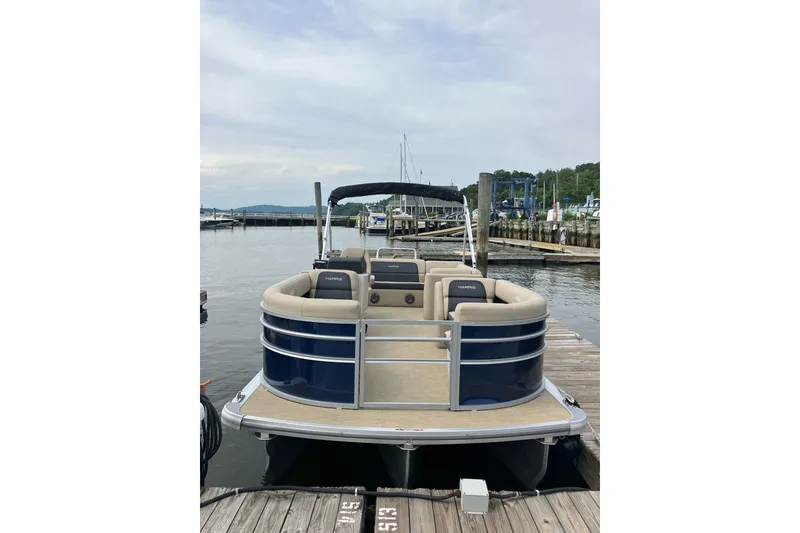 Slide: The Image of 2024 Harris Cruiser 230 pontoon boat docked at a marina, featuring beige seating and blue exterior. - 3